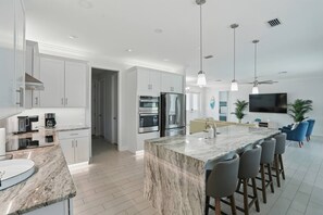 A modern kitchen with white cabinets, a marble island, and a dining area with bar stools.