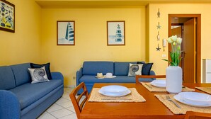 Ein Essbereich mit einem Holztisch, gedeckt für vier Personen, neben zwei blauen Sofas mit gemusterten Kissen.