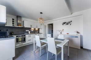 A modern kitchen with white cabinetry, a dining table with chairs, a built-in oven, and a hanging light fixture.