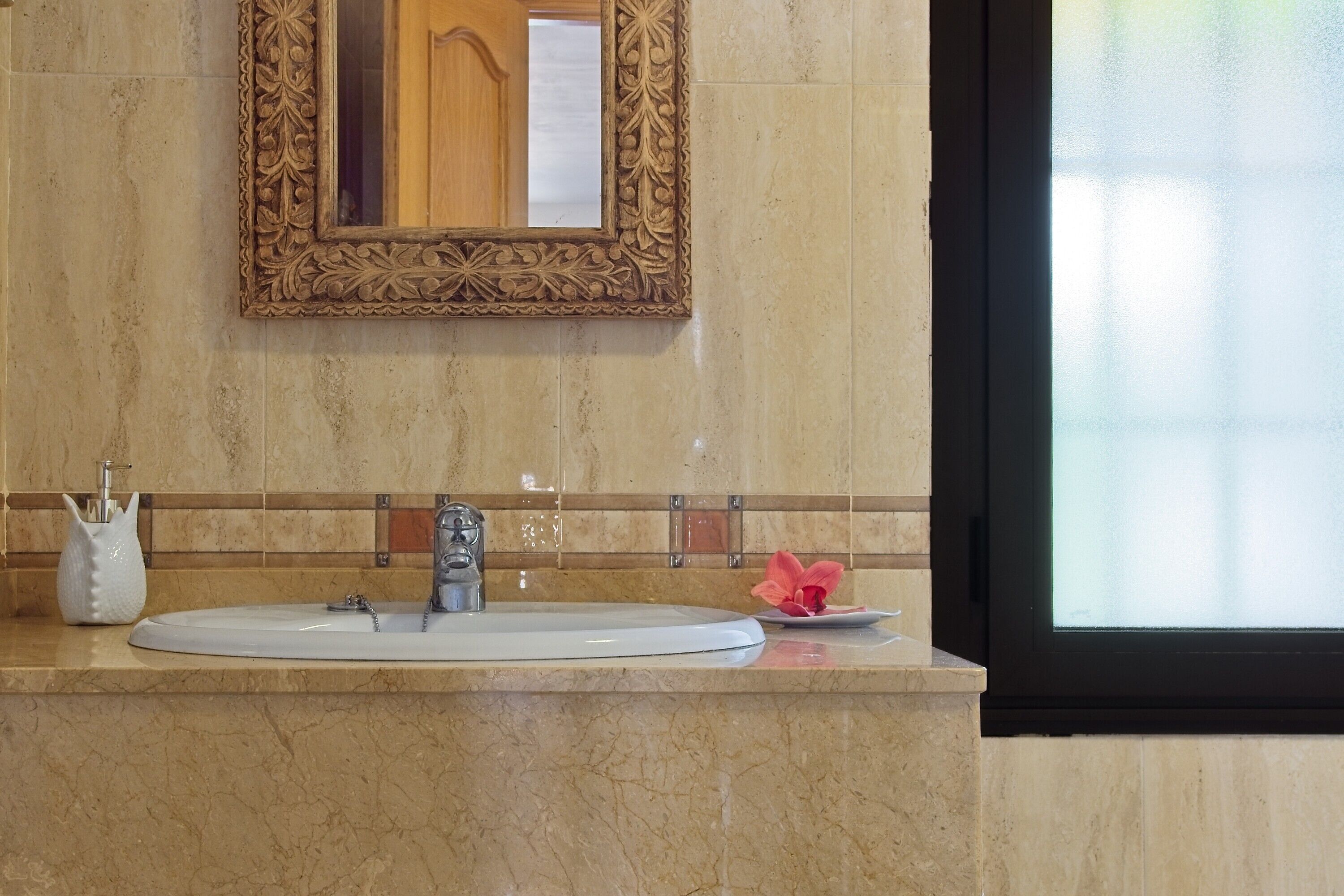 Un baño con lavamanos de mármol, un espejo decorativo y una ventana con vidrio esmerilado.