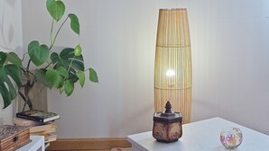 Huoneessa on valkoinen pöytä, ruukussa oleva kasvi, korkea lamppu ja koriste-esine.