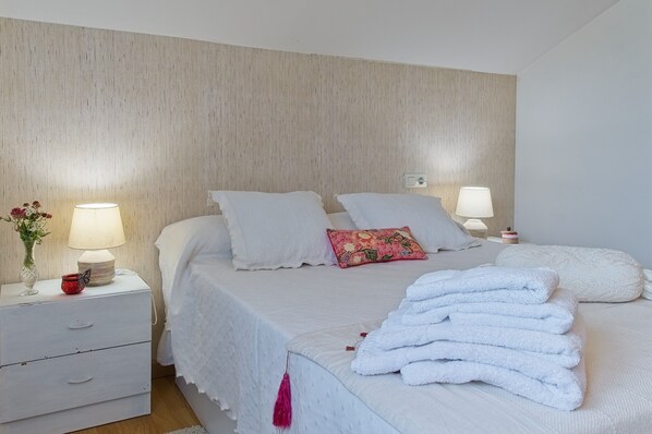 A neatly made bed with white linens, a bedside table with a lamp, and a wall with a textured finish. - Country House 'Kely' with Private Terrace, Private Garden and Wi-Fi (Antimio de Abajo)