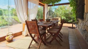 An outdoor dining area with a table and chairs, a hanging chair, and a basket of flowers.