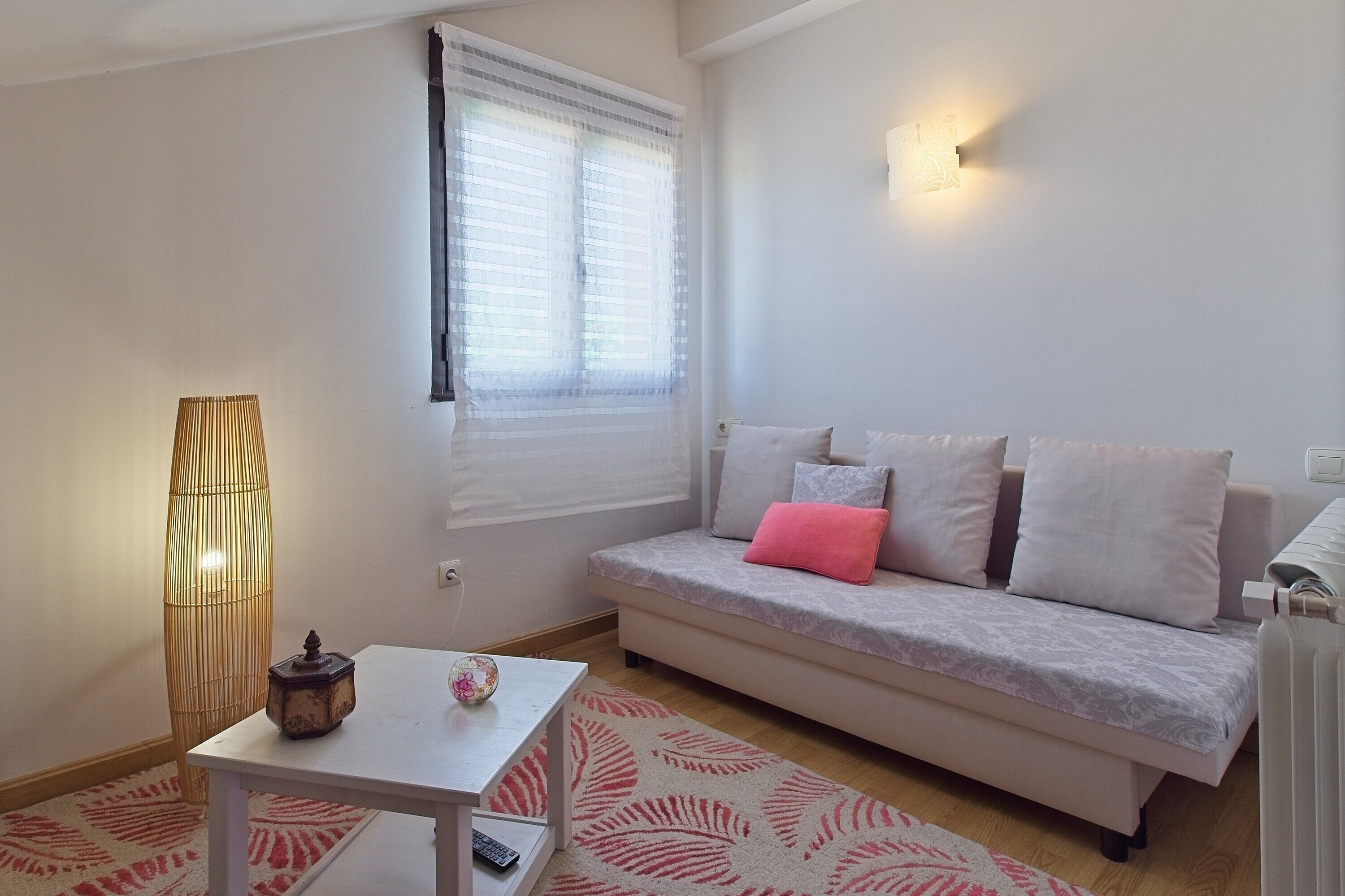 Un salon avec un canapé, une table, une lampe et une fenêtre avec des stores.