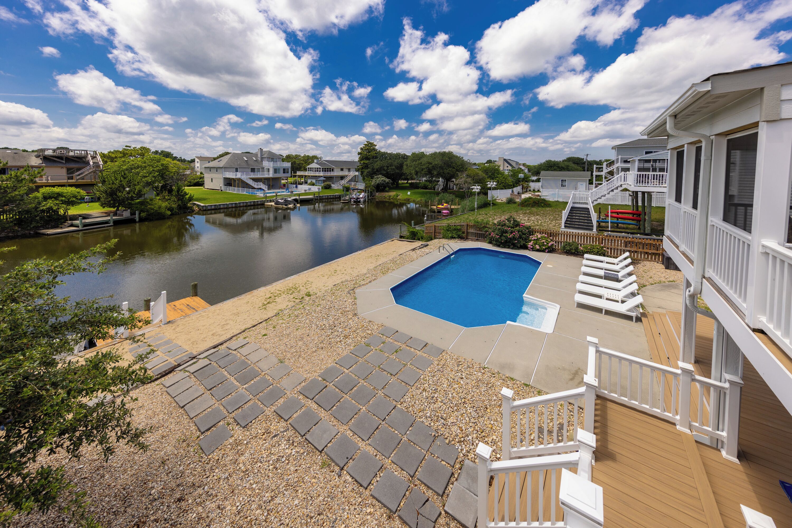 A backyard with a swimming pool, wooden deck, and a view of a lake.