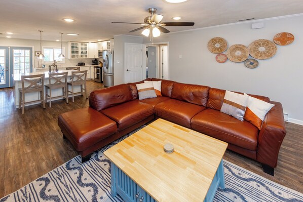 A spacious living room with a brown leather sectional sofa, a wooden coffee table, and a patterned rug.
