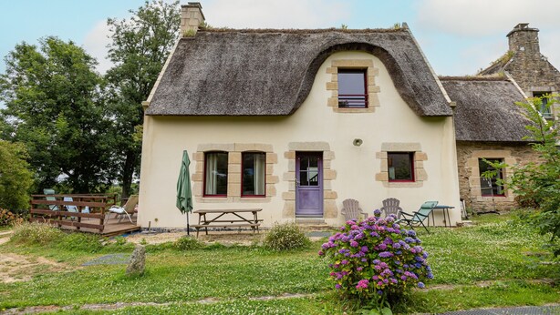 Ein traditionelles Haus mit einem Reetdach, einer Holzterrasse und einem kleinen Garten mit Blumen.