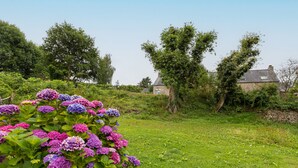 Ein Garten mit Hortensienbüschen, einer Steinmauer und einem Steinhaus mit Schornstein.