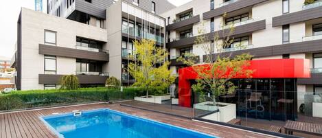 Un moderno edificio de apartamentos con piscina, balcones y un toldo rojo.