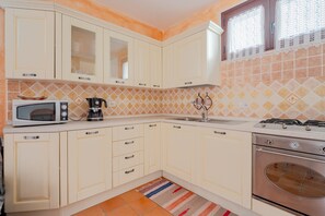 A kitchen with white cabinets, a microwave, a coffee maker, a gas stove, and a built-in oven. - Holiday Home 'Casa Spaziosa' with Air Conditioning (Bari Sardo)