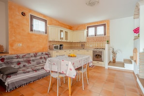 A compact kitchen with white cabinets, a dining table with chairs, a sofa, and a small staircase. - Holiday Home 'Casa Spaziosa' with Air Conditioning (Bari Sardo)
