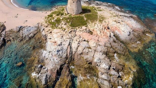 A rocky island with clear blue waters, a sandy beach, and a stone structure. - Holiday Home 'Casa Spaziosa' with Air Conditioning (Bari Sardo)