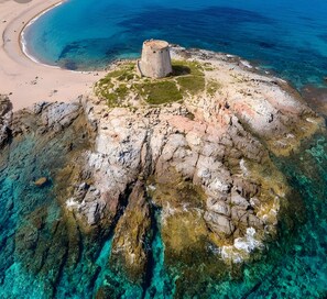 Une île rocheuse aux eaux d’un bleu limpide, avec une plage de sable et une structure en pierre.