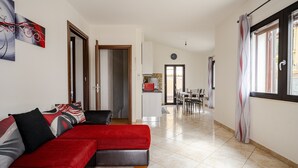 A modern living room with a red sofa, a dining area with a table and chairs, and a kitchen in the background. - Holiday Home 'Casa Spaziosa' with Air Conditioning (Bari Sardo)