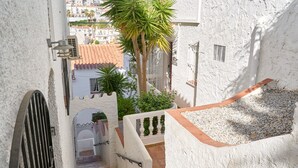 A narrow outdoor corridor with a metal gate, a palm tree, and a staircase leading to an upper level. - Holiday Home 'Casa Del Sol' with Sea Views, Wi-Fi and Air Conditioning (Nerja)