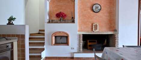 A kitchen with a brick oven, a clock, and a staircase leading to another level.