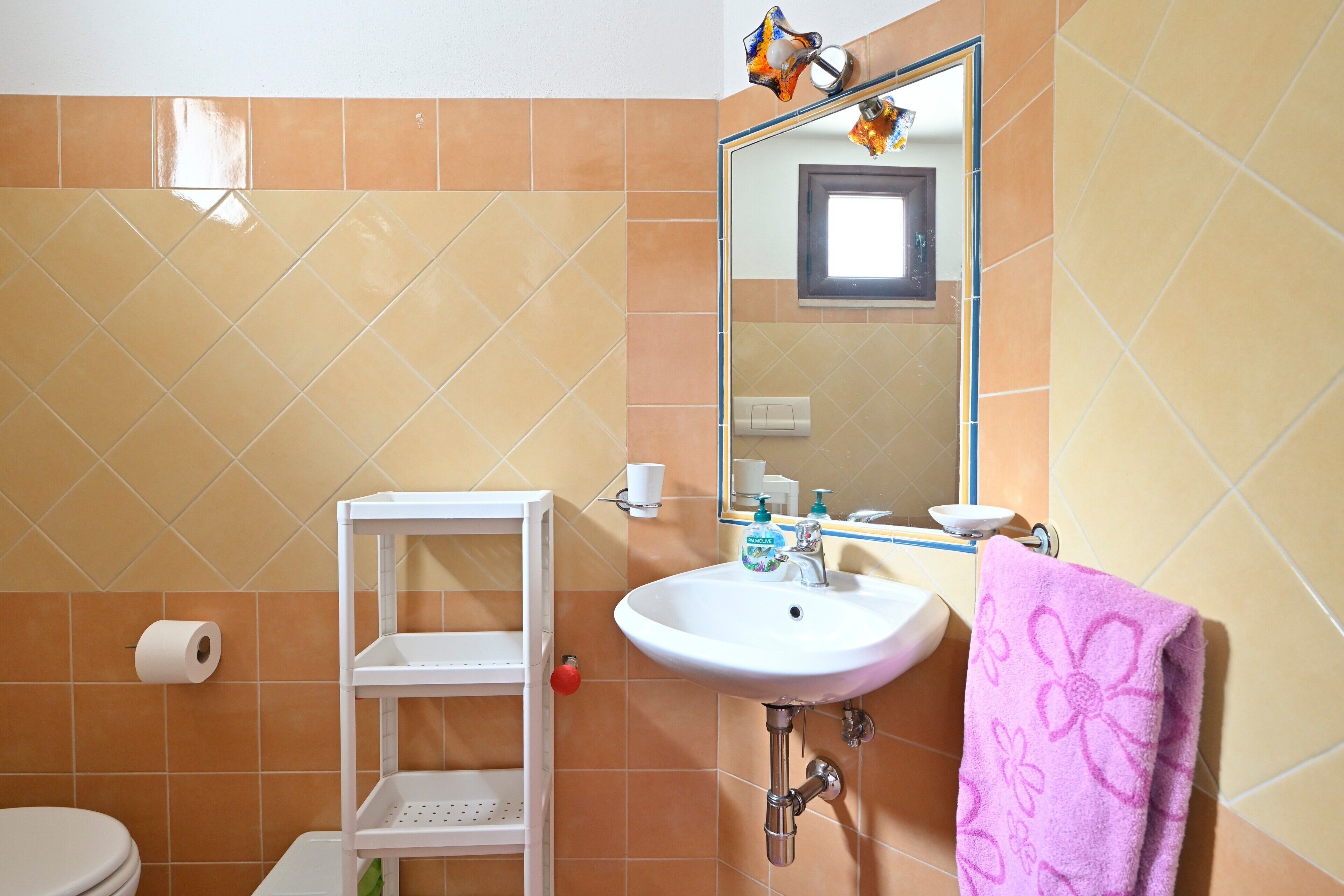 A bathroom with a white sink, a mirror, a toilet, and a shelf with a red object.