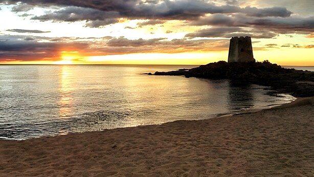 Un coucher de soleil sur la côte, avec une tour perchée sur un promontoire rocheux.