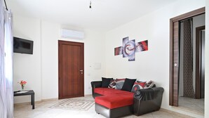 Uma sala de estar com sofá, televisão, uma porta e parede com uma obra de arte abstrata.