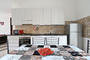 Una cocina con armarios blancos, microondas, estufa y refrigerador.
