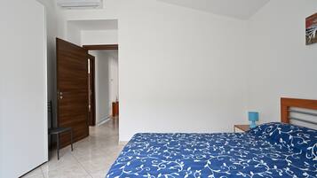 Ein Schlafzimmer mit Bett, Stuhl, Holztür, weißer Wand und einem kleinen Tisch mit Lampe.