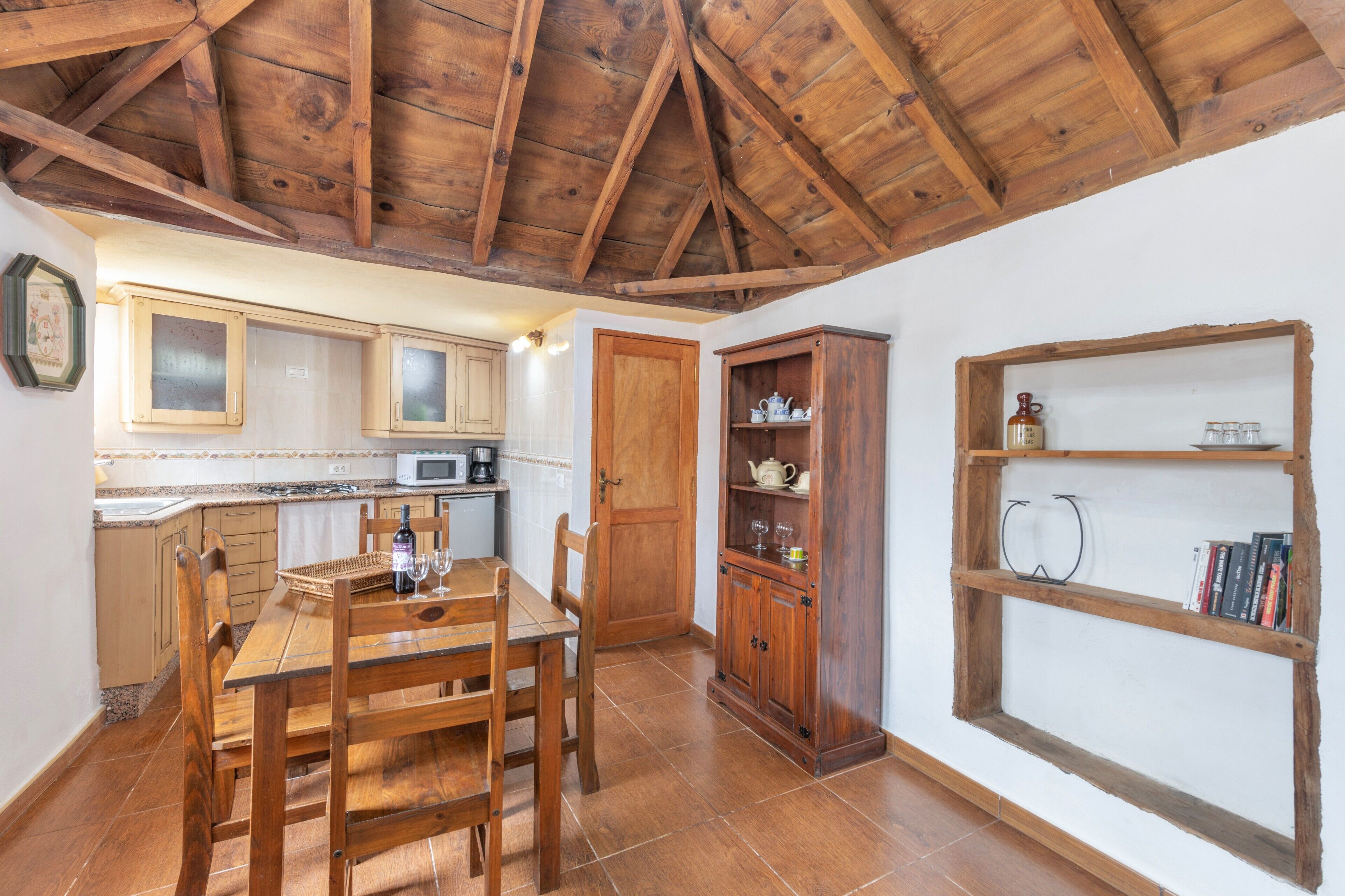 Une cuisine rustique avec des poutres en bois, une table à manger avec des chaises, un four à micro-ondes et un meuble avec des étagères.
