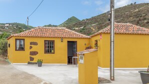 A yellow building with a tiled roof, a concrete driveway, and a hillside in the background. - Holiday Home 'La Rehoya' with Sea View, Private Terrace and Wi-Fi (Puntallana)