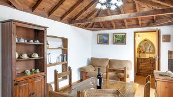 A wooden dining table with chairs, a wooden cabinet with shelves, a sofa, and a chandelier.