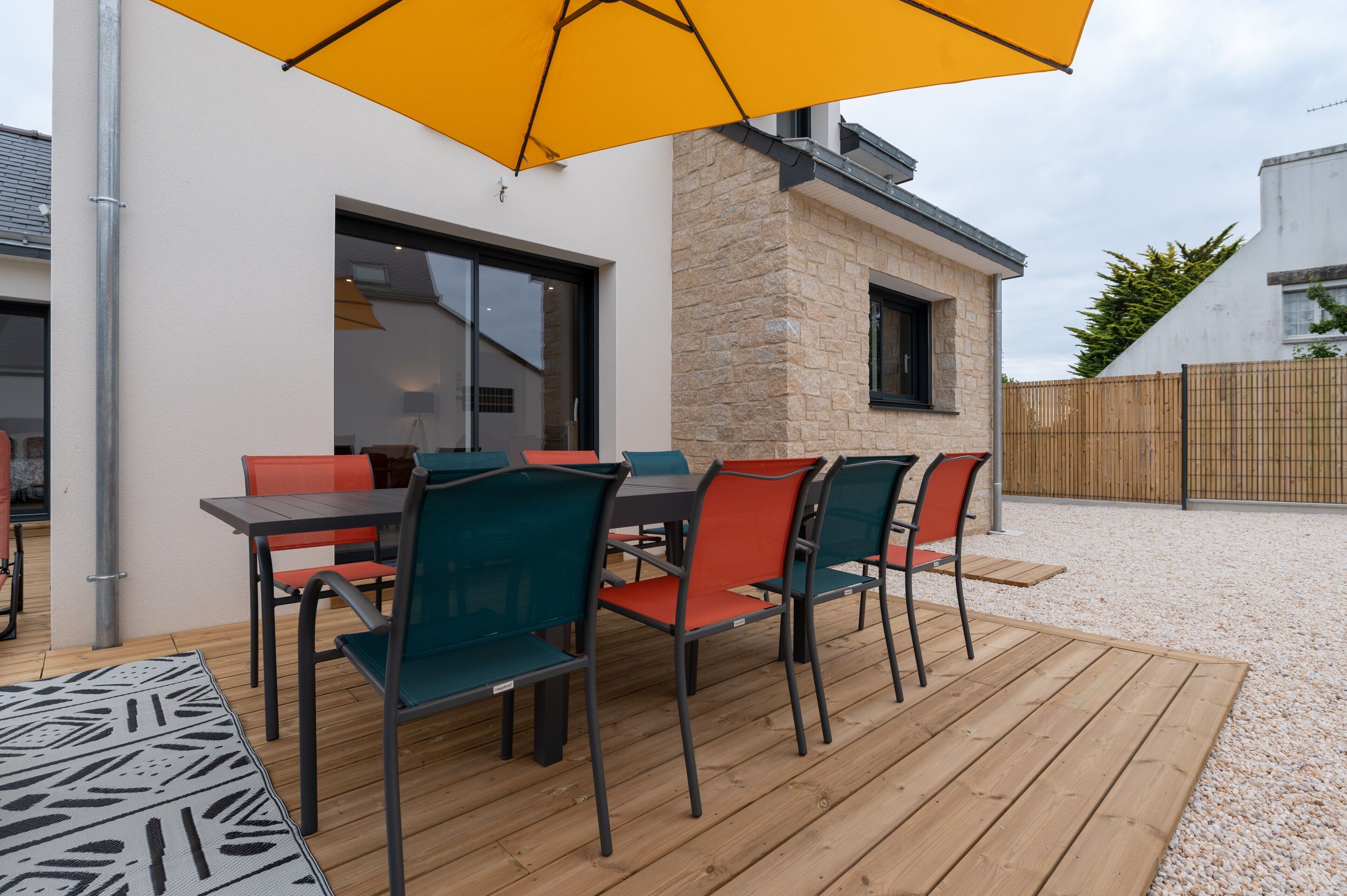 An outdoor dining area with a wooden deck, a table with chairs, and a yellow umbrella.