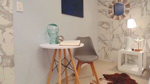 Ein modernes Zimmer mit Wand im Marmoroptik, einem runden Tisch mit Buch und Vase, einem grauen Sessel, einem kleinen weißen Beistelltisch mit Lampe und einem Kuhfellteppich.