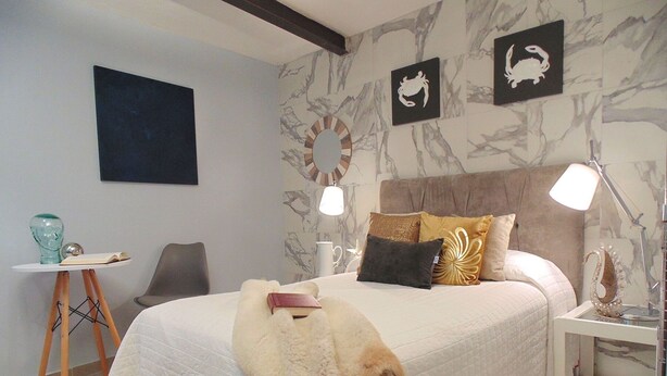 Ein Schlafzimmer mit einem großen Bett, einem Nachttisch, einem Sessel und einer Wand mit Dekoration.