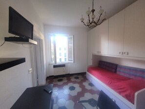 Una stanza piccola con un letto, una scrivania, una sedia, una TV e una finestra.