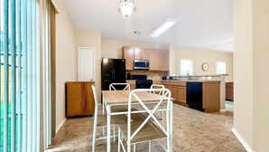 A modern kitchen with a dining area, featuring a white metal table and chairs, a refrigerator, microwave, stove, and wooden cabinets.