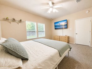 Ein Schlafzimmer mit einem Bett, einem Deckenventilator, einem Fernseher, einem Schminktisch und einer Tür.