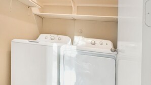 A laundry room with two white front-loading washing machines and a white shelf above them.