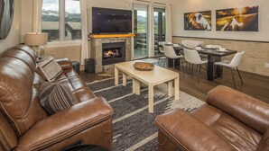 A living room with a fireplace, leather sofas, a dining area with a table and chairs, and a large TV.