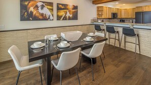 A modern kitchen with wooden cabinets, a central island, and a dining area with a dark table and white chairs.