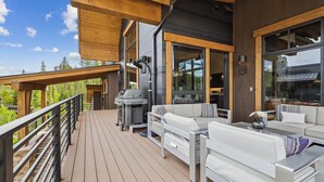 A deck with a grill, outdoor seating, and large windows overlooking a forested area. - Chateau Breck: Luxury Townhome, Hot Tub & Fire Pit, Five-Peak Views. (Breckenridge)