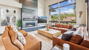 A spacious living room with a fireplace, leather sofas, and large windows offering mountain views. - Chateau Breck: Luxury Townhome, Hot Tub & Fire Pit, Five-Peak Views. (Breckenridge)
