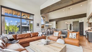 A spacious living room with a large leather sectional sofa, a wooden coffee table, and a dining area with a chandelier. - Chateau Breck: Luxury Townhome, Hot Tub & Fire Pit, Five-Peak Views. (Breckenridge)