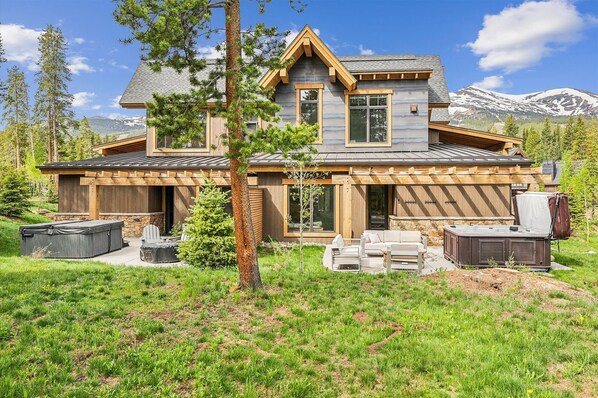 Une maison moderne à deux étages, dotée de fondations en pierre, de grandes fenêtres et d’une terrasse en bois.