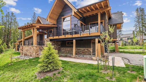 A modern two-story house with a stone foundation, wooden beams, and a balcony with a metal railing. - Chateau Breck: Luxury Townhome, Hot Tub & Fire Pit, Five-Peak Views. (Breckenridge)
