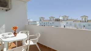Un balcón con una mesa y sillas blancas, una planta en maceta y vistas a edificios con tejados de tejas.