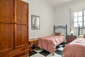 A bedroom with two beds, a wooden wardrobe, a bedside table, a lamp, and a framed picture on the wall.