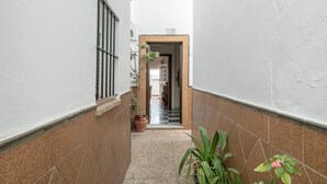 Un pasillo estrecho con suelo de baldosas, plantas en macetas y una puerta con el número 15.