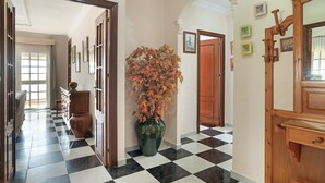 Un pasillo con piso de cuadros, puertas de madera, un jarrón con hojas otoñales y cuadros en las paredes.