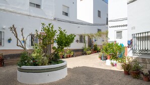 Un patio con una jardinera circular, plantas en macetas y un edificio blanco con ventanas y balcones.