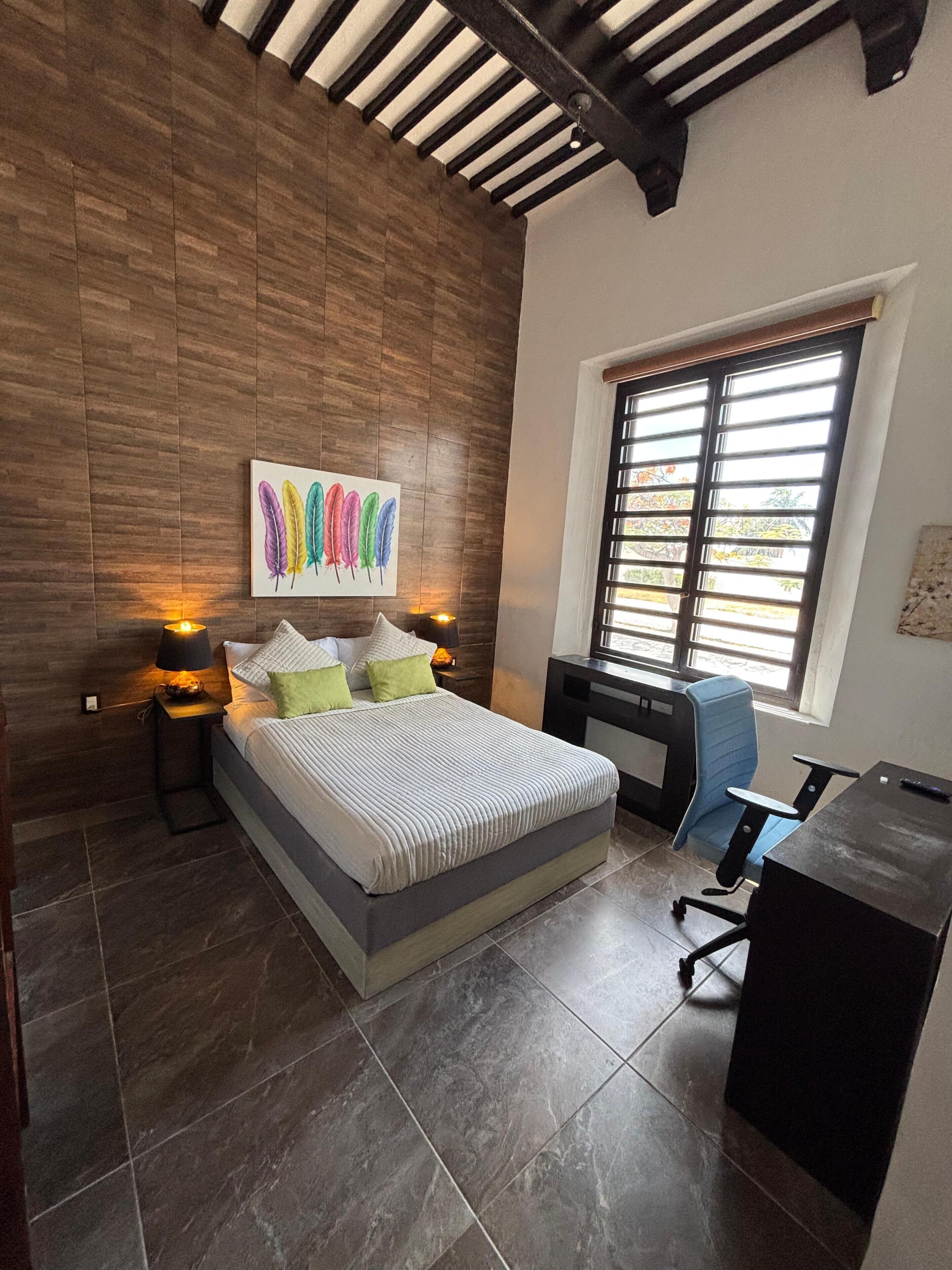 A bedroom with a bed, bedside lamps, a desk, and a chair.