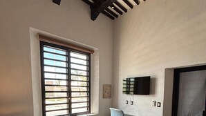 Un dormitorio con cama, escritorio, silla, televisor y ventana con persianas.