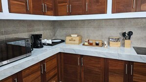Una cocina con armarios de madera, microondas, cafetera y diversos utensilios de cocina sobre la encimera.